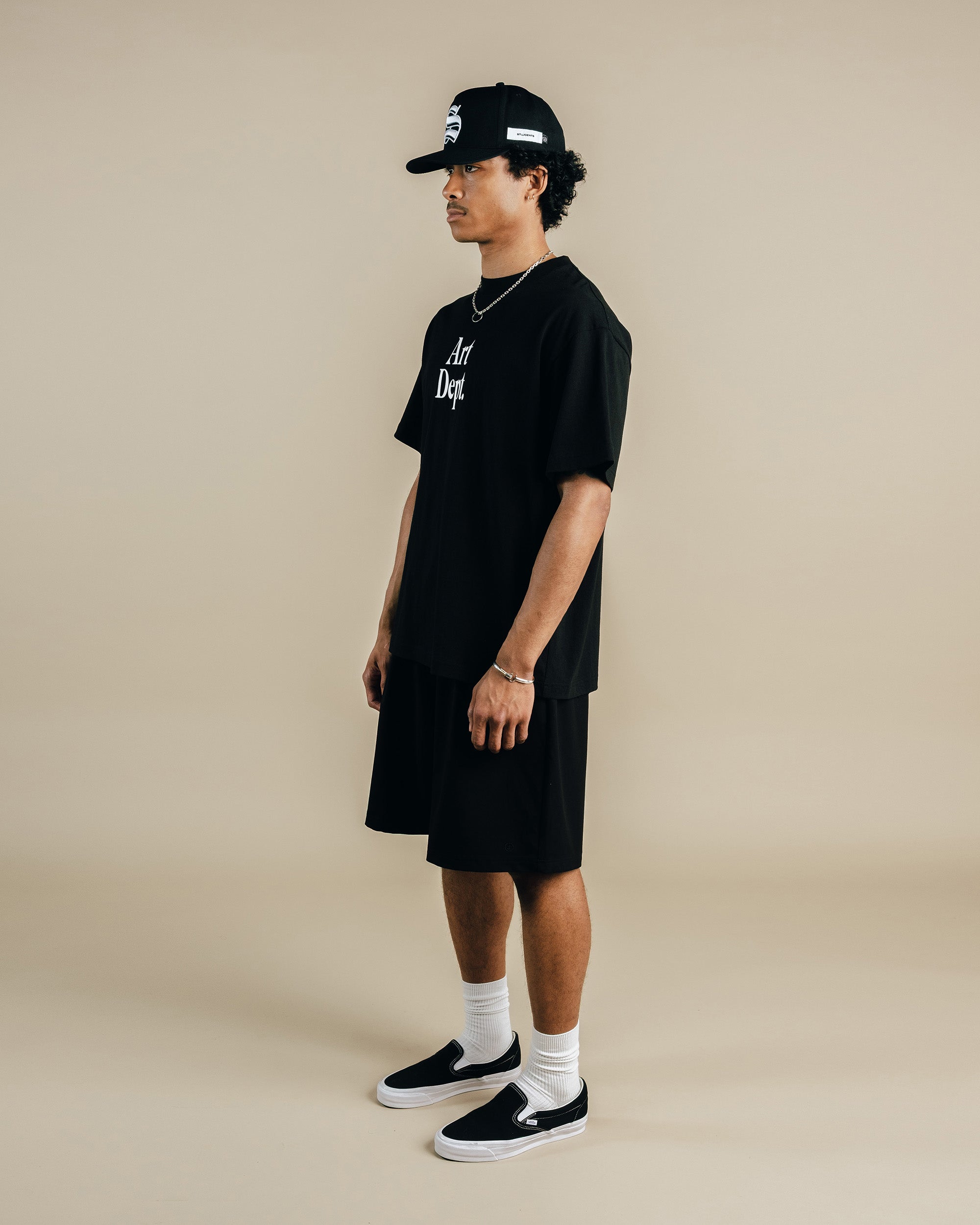 Person wearing a black t-shirt, shorts, and cap on a beige background
