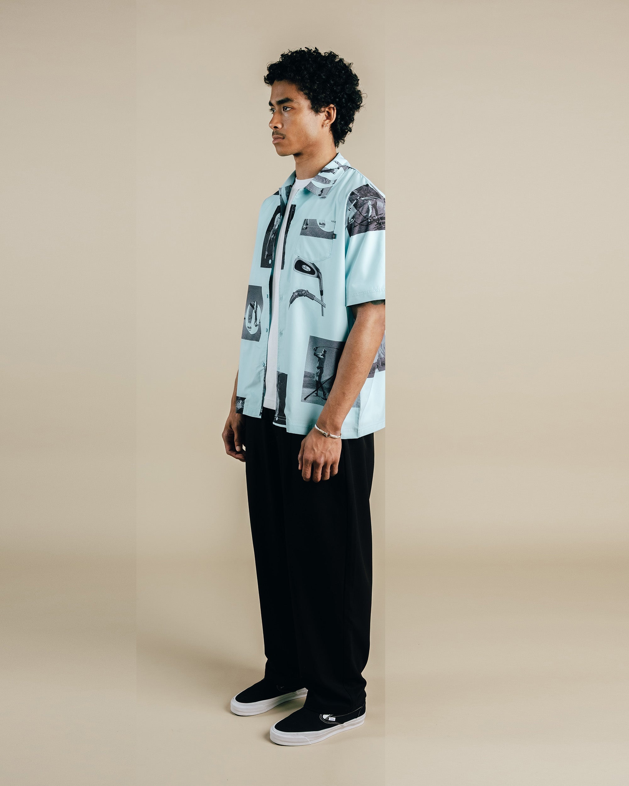 Man wearing a light blue patterned shirt and black pants on a beige background