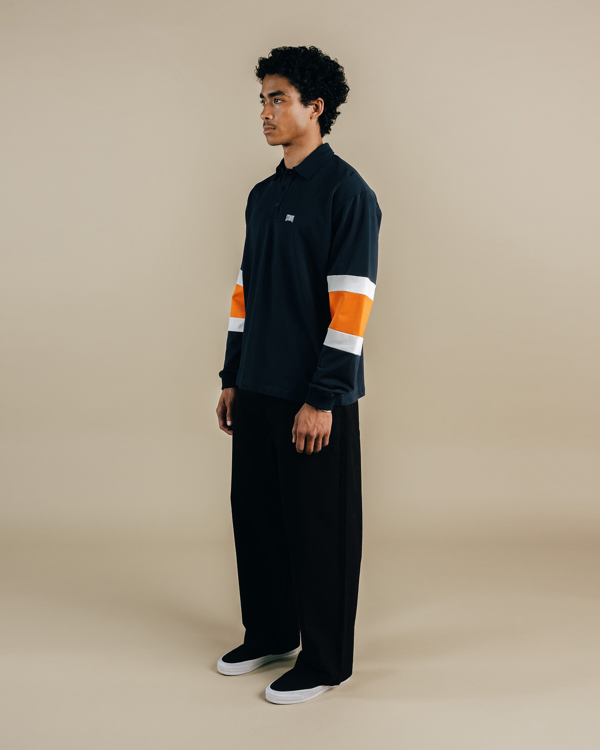 Person wearing a black outfit with orange and white stripes on a beige background