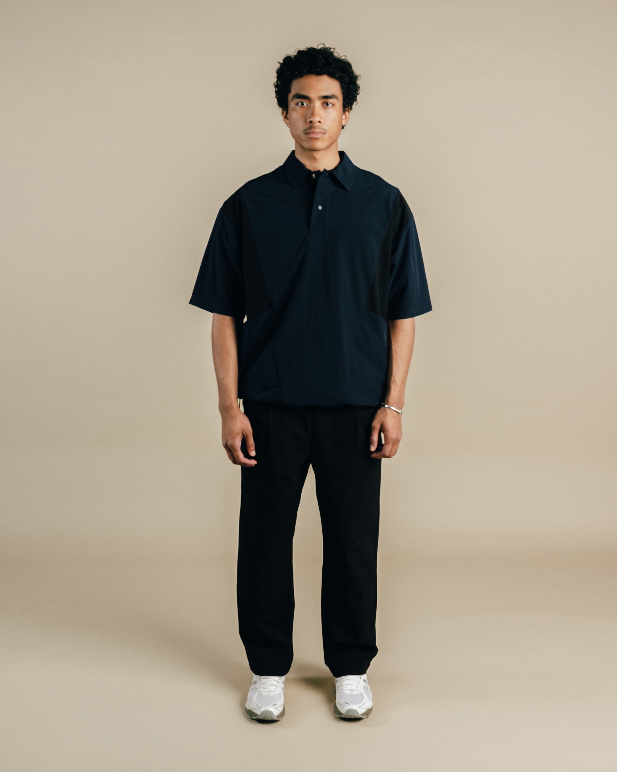 Man wearing a black polo shirt and pants on a beige background