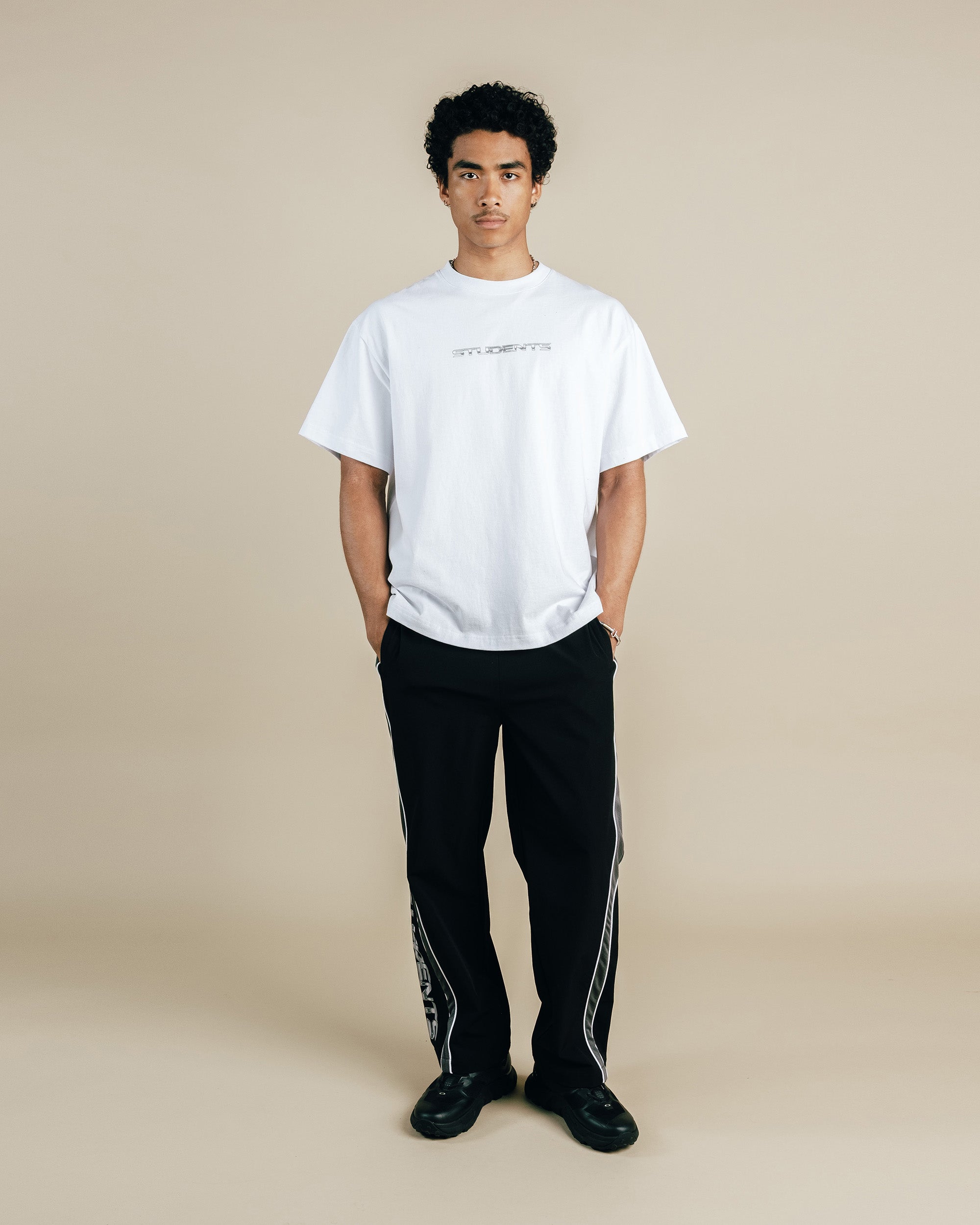 Person wearing a white t-shirt and black pants with a stripe on a beige background