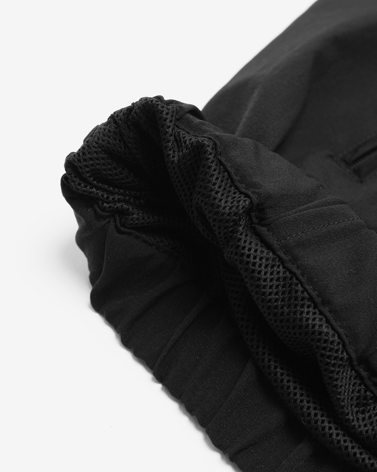 Close-up detail of a black garment showing a gathered elastic cuff with a breathable mesh lining on a white background.