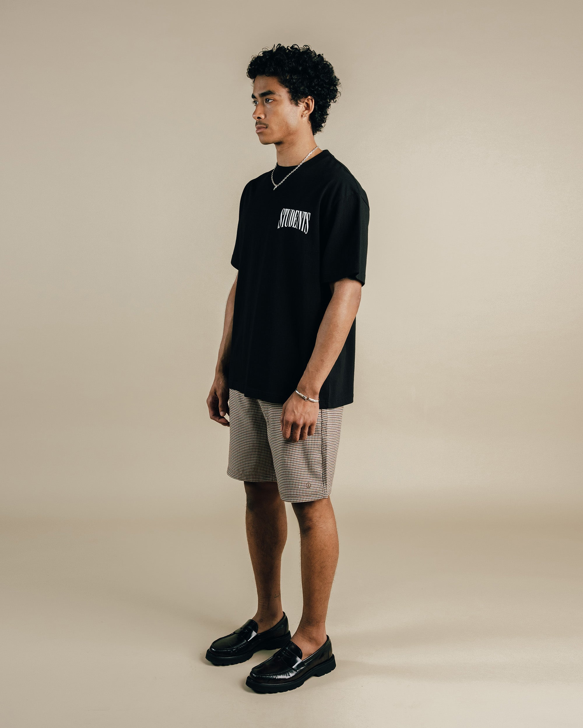 Man wearing a black t-shirt with text and brown shorts on a plain background