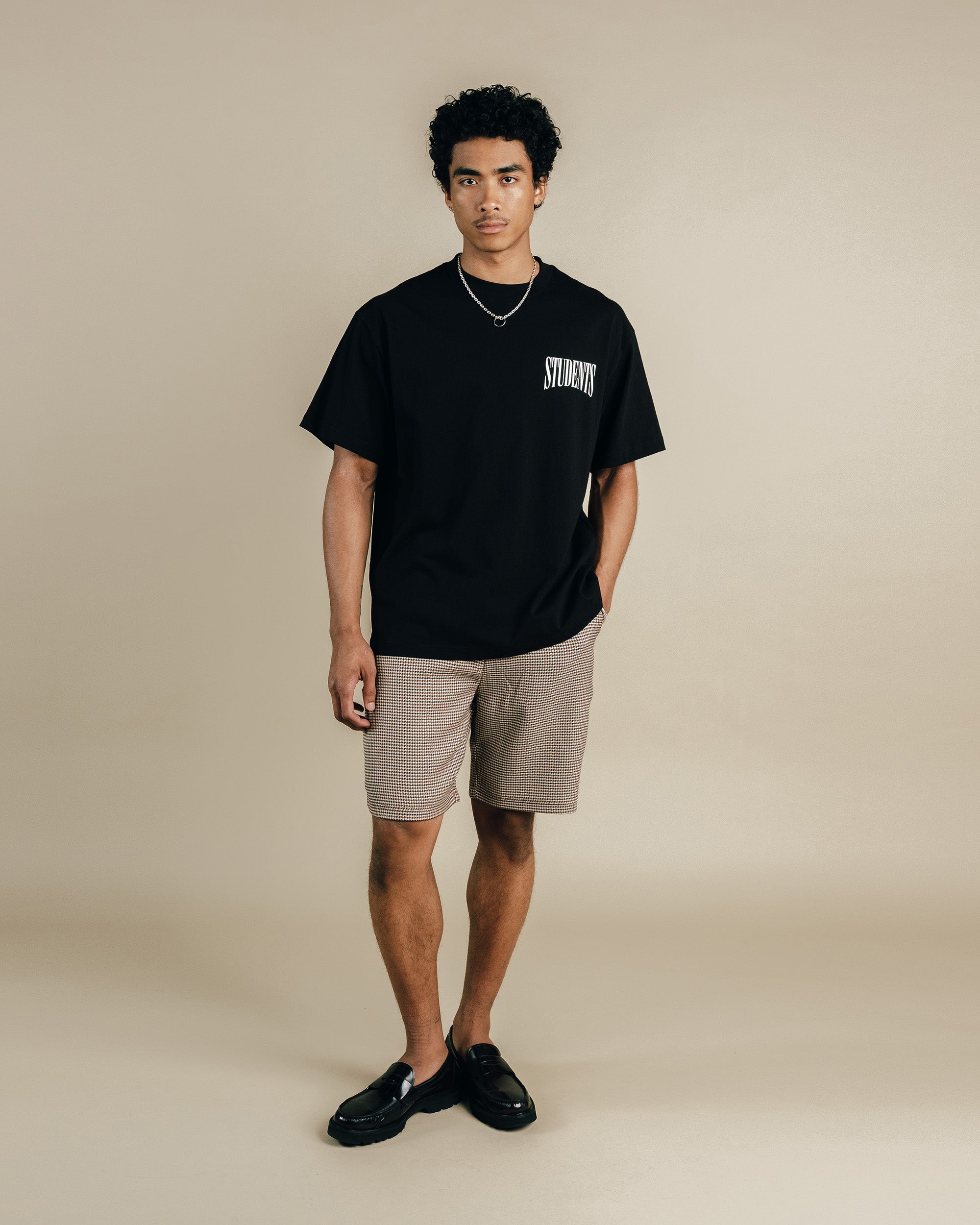 Man wearing a black t-shirt with text and beige shorts on a beige background