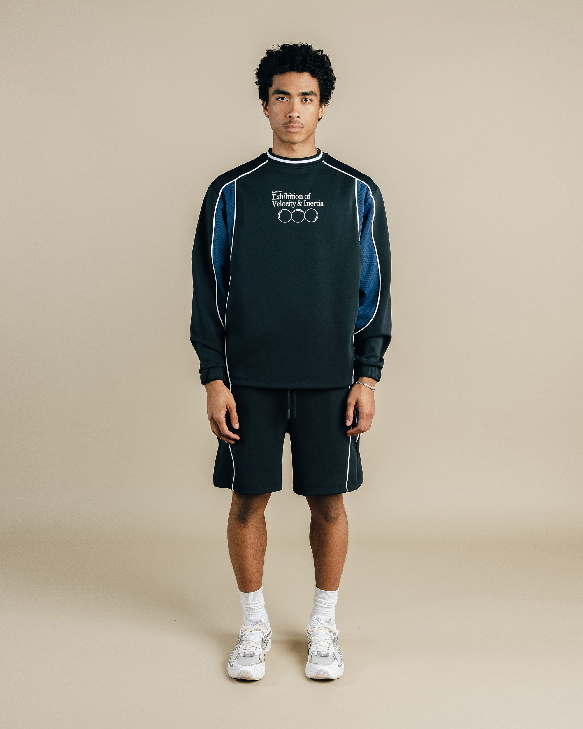 Person wearing a black and blue tracksuit with visible branding on a beige background