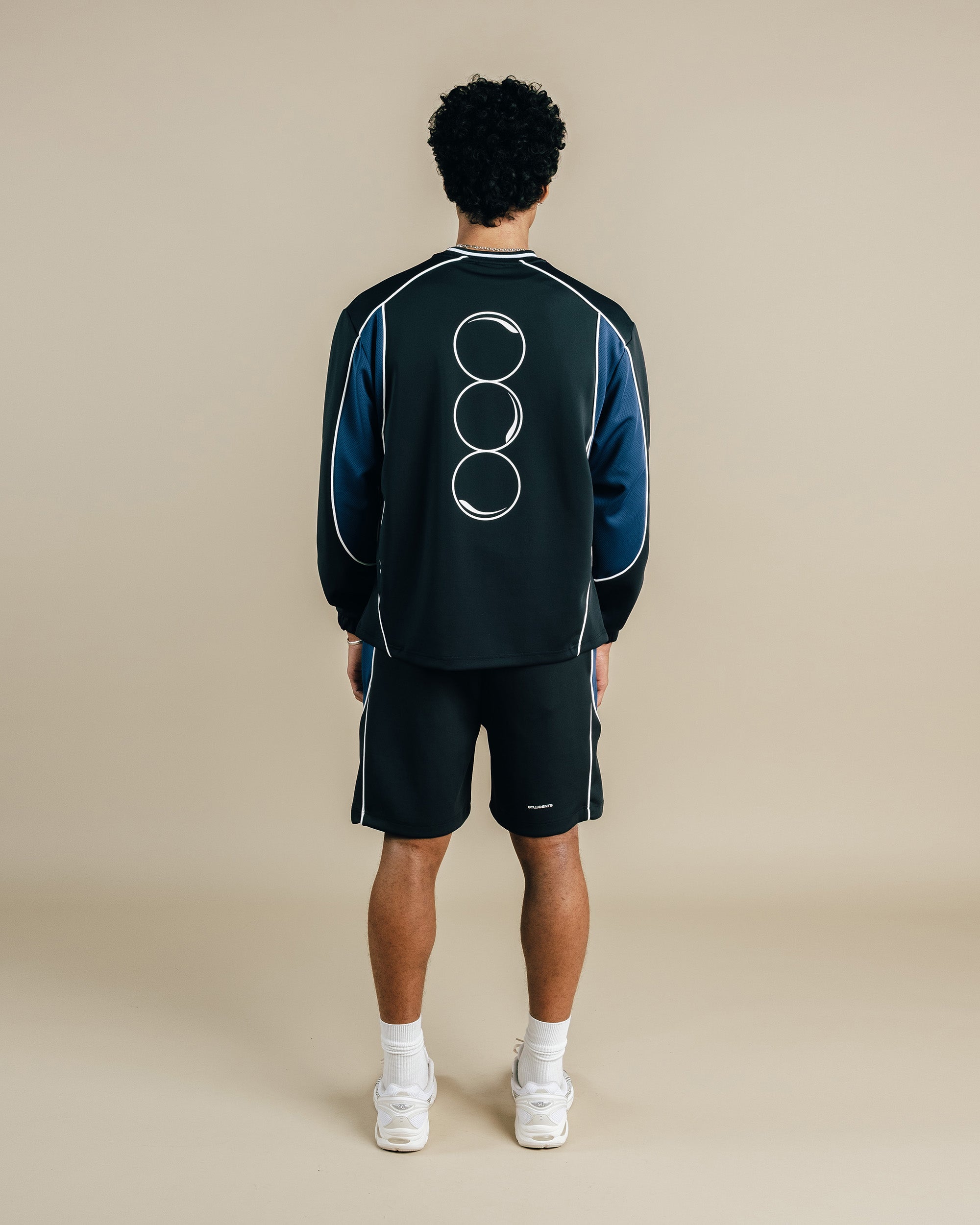 Person wearing a black tracksuit with a logo on the back against a beige background