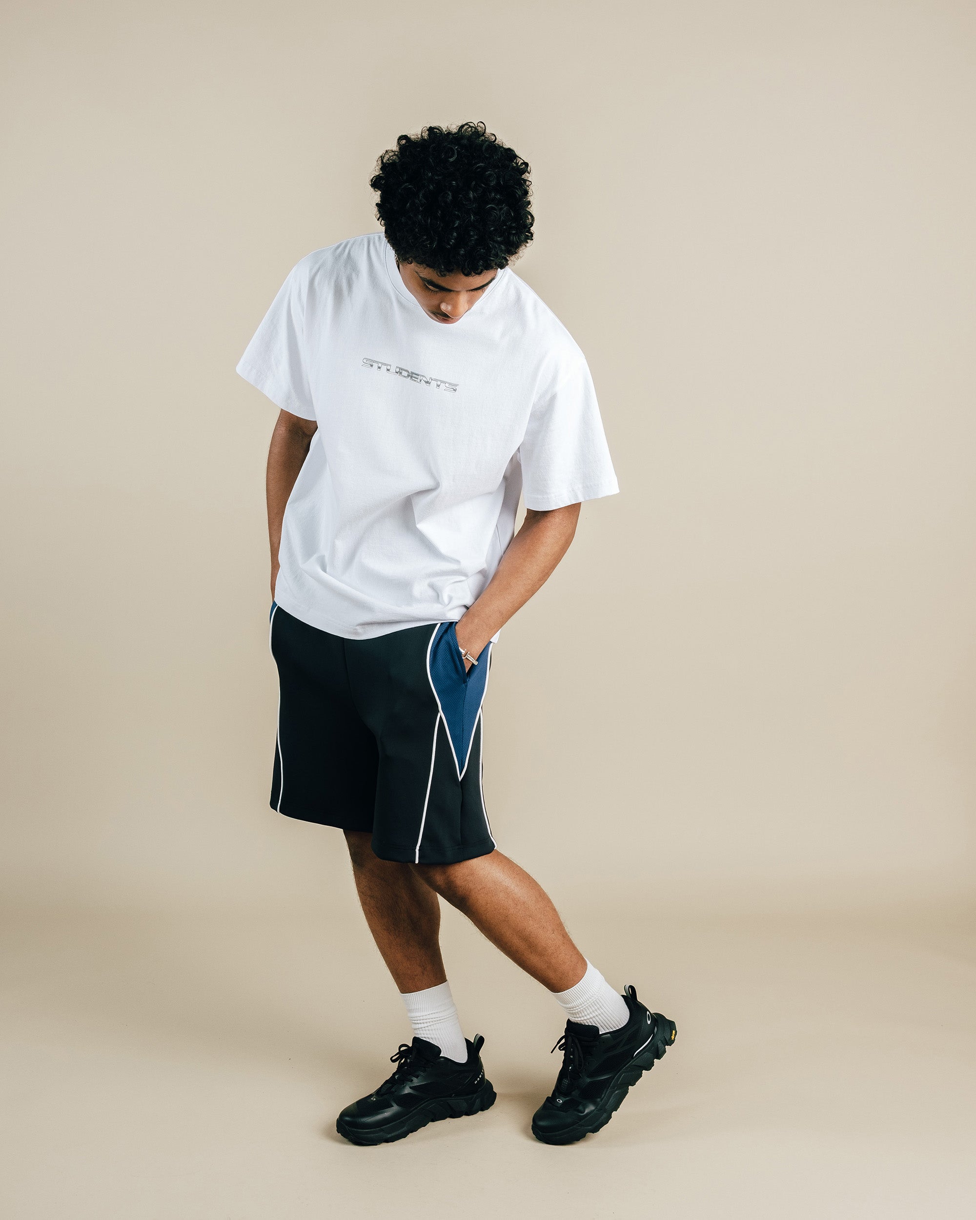 Person wearing a white t-shirt, black shorts, and black shoes on a beige background
