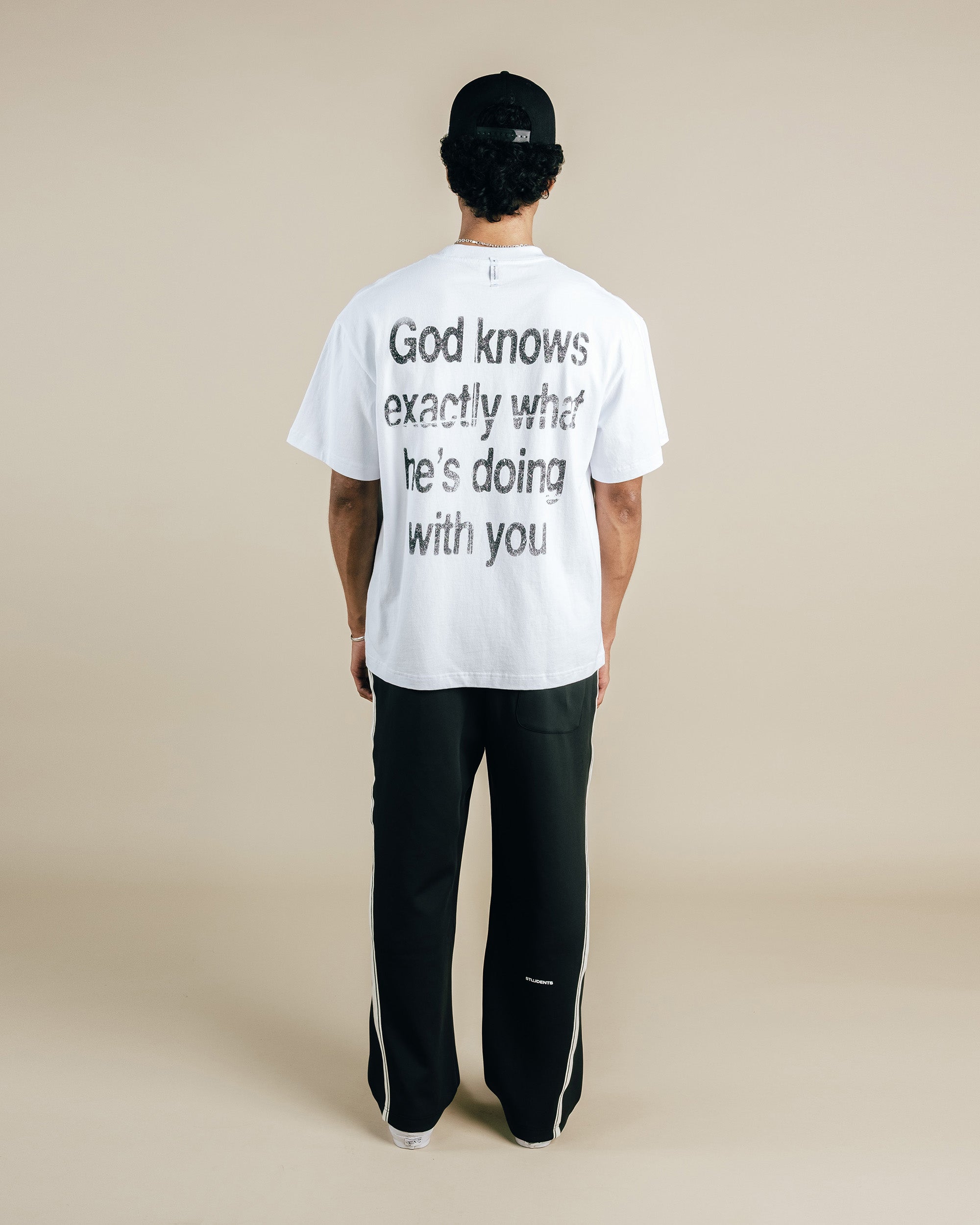 Person wearing a white t-shirt with text on the back, standing against a beige background