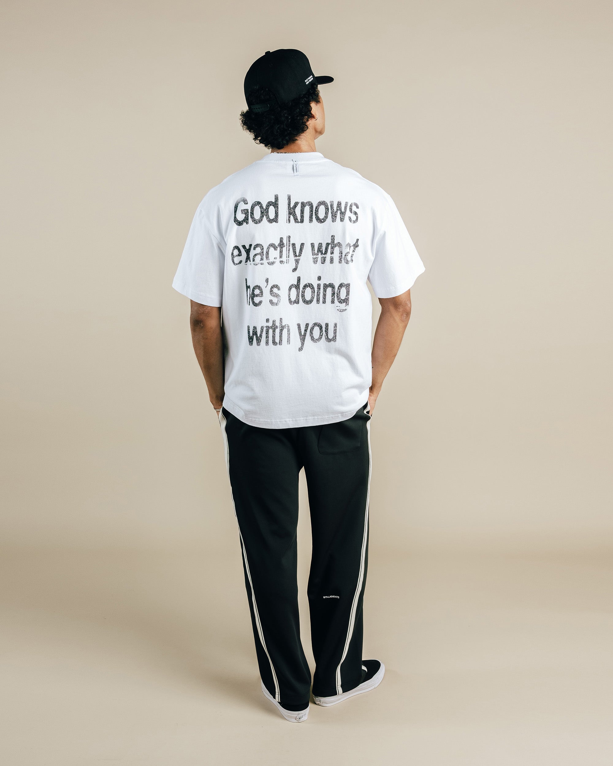 Person wearing a white t-shirt with text on the back, standing against a beige background