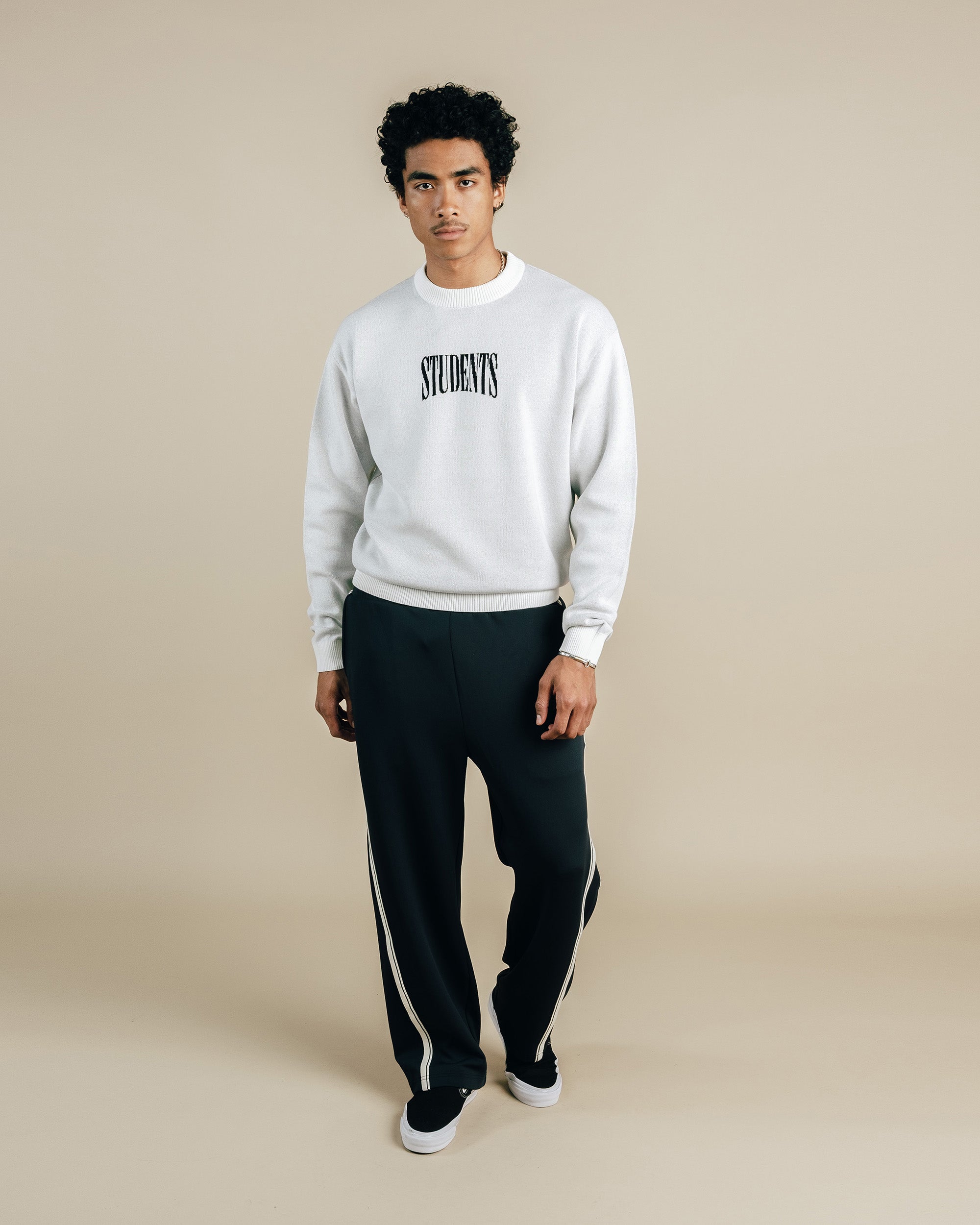 Person wearing a white sweatshirt with 'STUDENT' text and black pants on a beige background