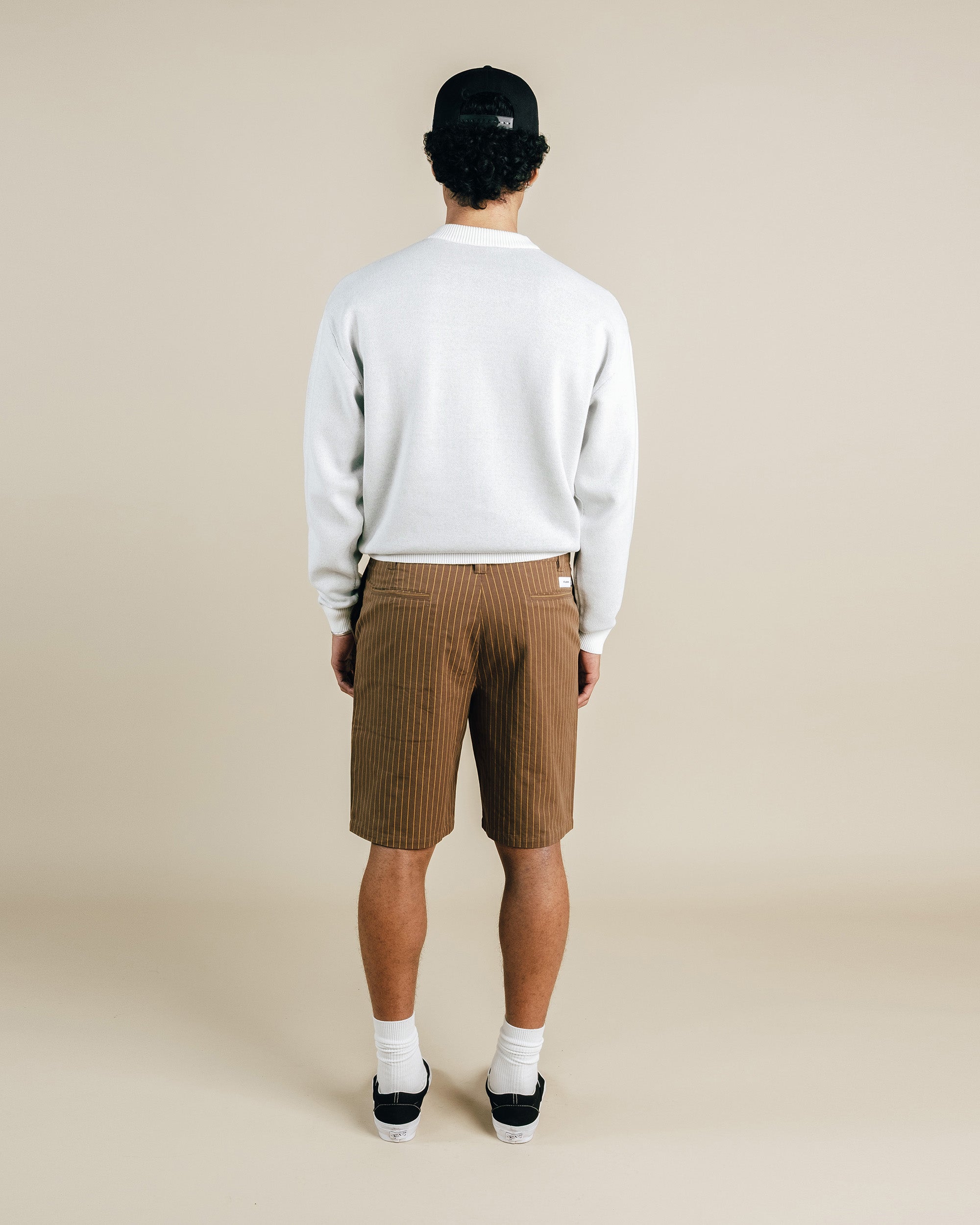 Person wearing a white sweater and brown shorts on a beige background