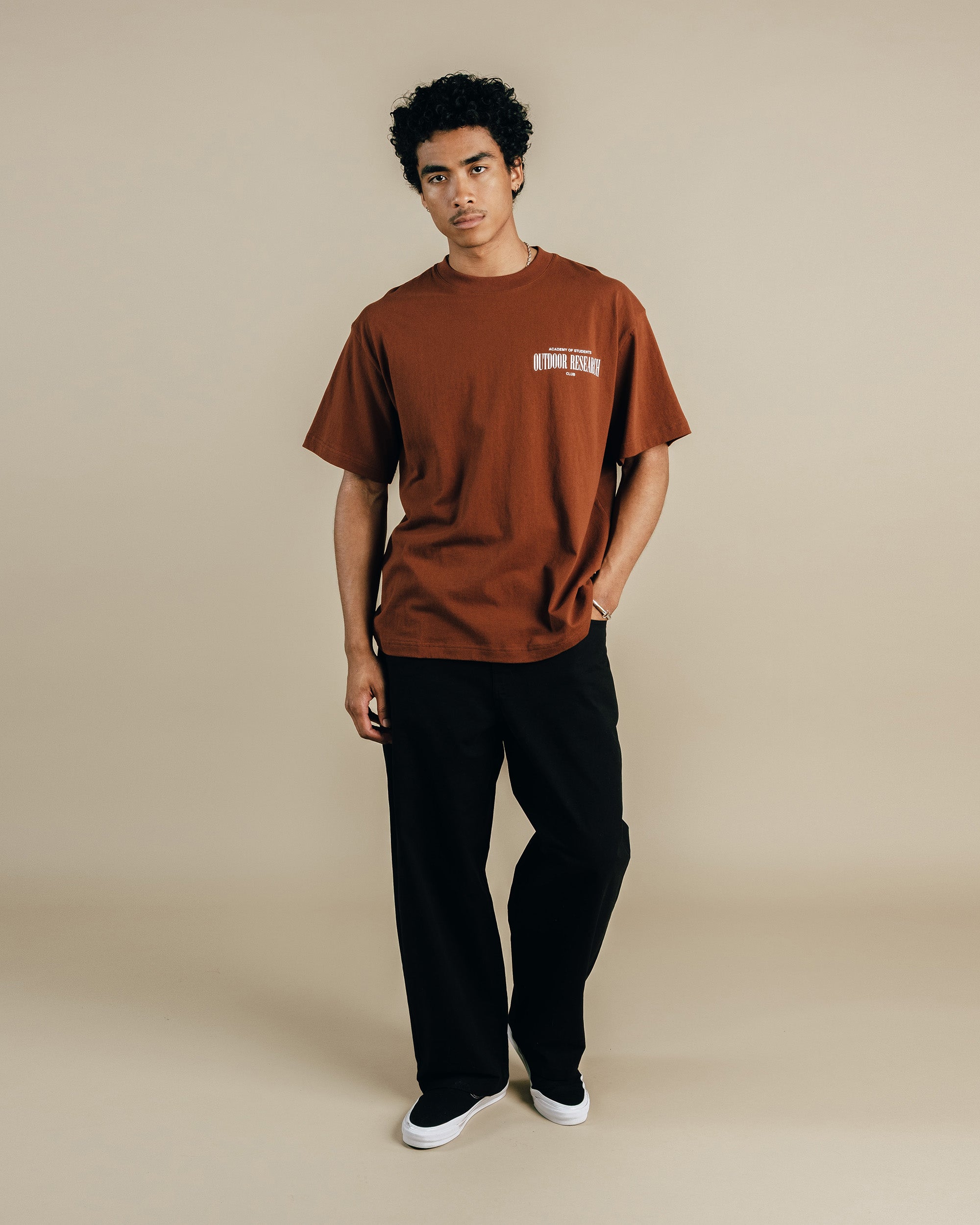 Person wearing a brown t-shirt and black pants on a beige background
