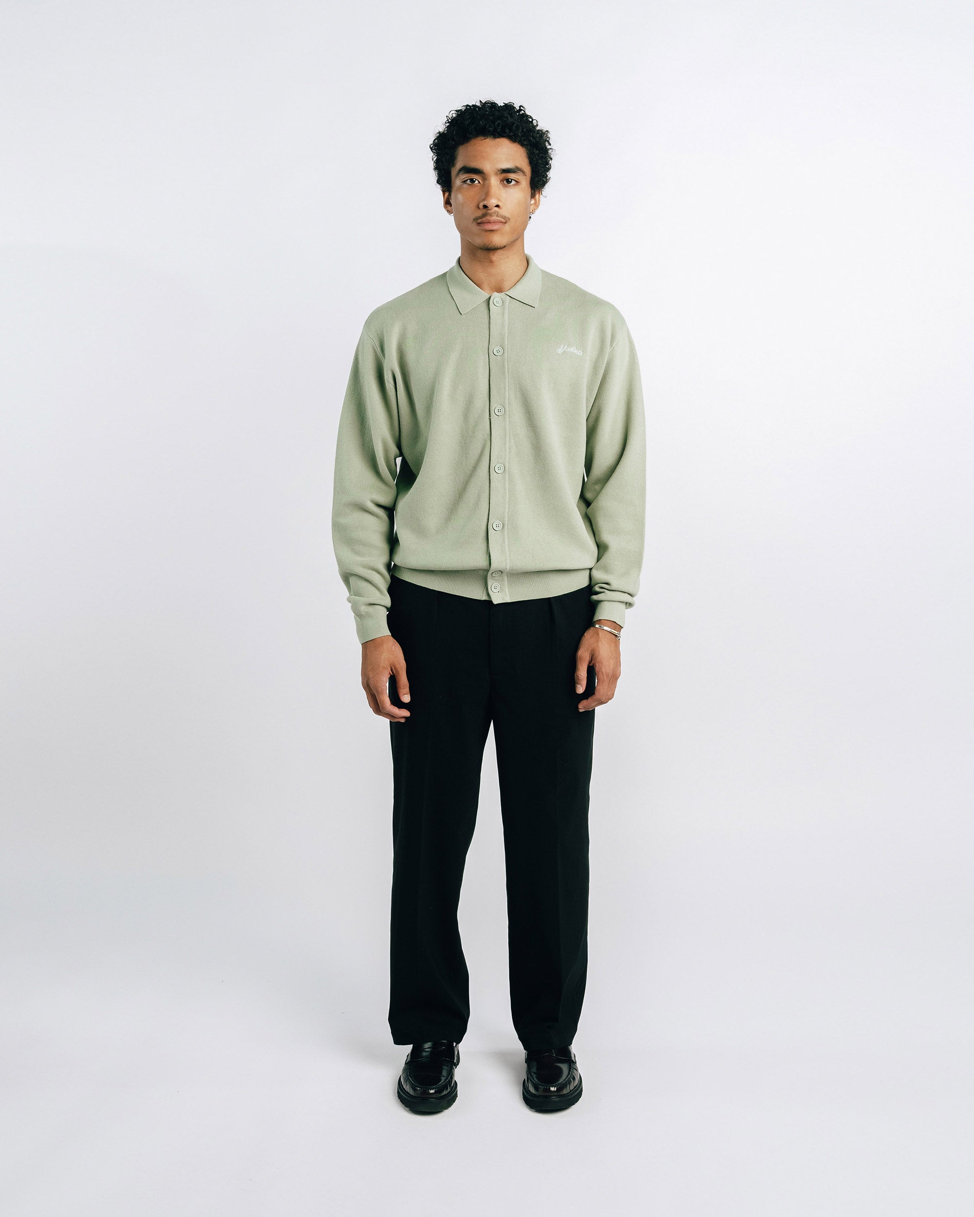 Person wearing a light green jacket and black pants on a white background